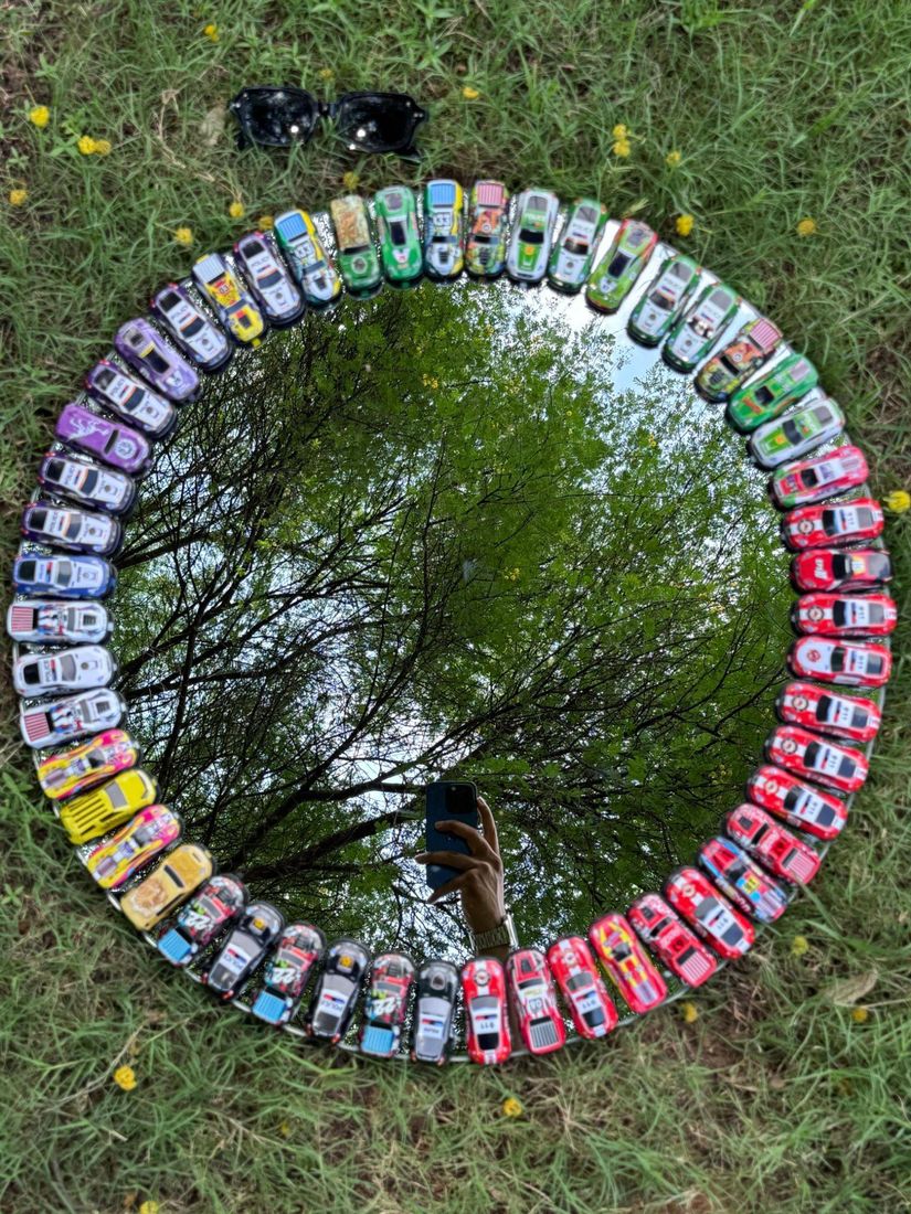 Round mirror ringed bumper to bumper with colorful toy cars, on grass