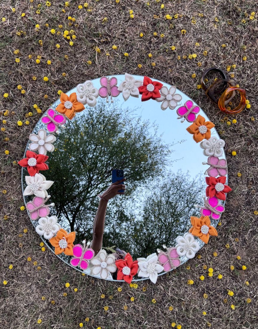 Round mirror edged with crochet flowers and butterflies, lying on dry grass