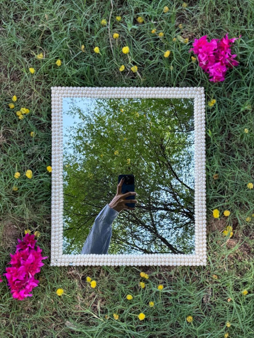 Rectangular mirror framed in rows of white pearl beads, on grass with pink flowers